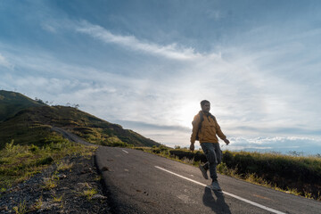 Obraz premium A man in outdoor gear walks confidently along a mountain road, holding a smartphone. The morning light and empty road highlight a sense of purpose, solitude, and discovery.