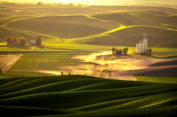 Drone photo of farm lands rolling hills with glowing dust from the country road and an elevator....