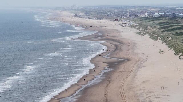 people walking the beach along the water line. Dunes, sand, recreation and leisure.Aerial video.