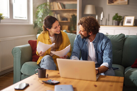 A couple sits together on their couch discussing various life insurance plans. They review important documents while a laptop is open on the coffee table, creating a warm atmosphere.