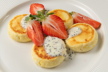 Delicious golden cheesecakes, also known as syrniki, served with sweet poppy seed sauce and fresh, juicy strawberry slices, creating a tempting breakfast or dessert