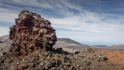 Volcanic rock formation stands prominently against a backdrop of rugged terrain and distant...