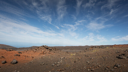 Barren volcanic landscape with rugged terrain, scattered rocks, and vibrant earth tones under a...