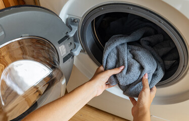 Housewife taking clothes out of washing machine. Modern woman housekeeper putting dirty clothes in...
