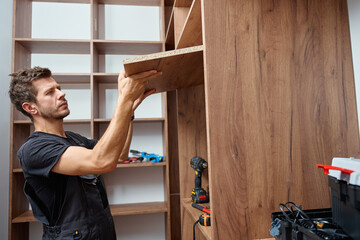 Man assembling wooden wardrobe at home using tools and holding large wooden panel. Concept of DIY...