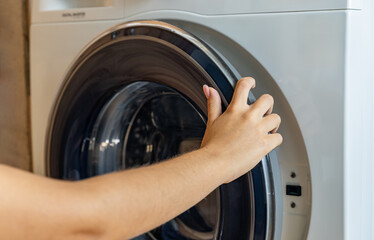 Housewife taking clothes out of washing machine. Modern woman housekeeper putting dirty clothes in...