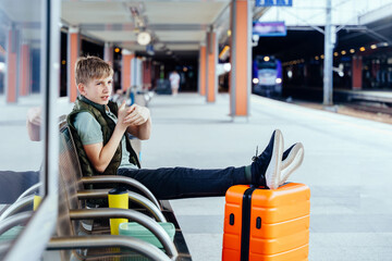 Teenage boy with orange suitcase waiting for train transfer