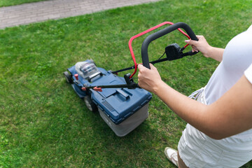 This image captures someone mowing their lawn with a push lawn mower. The person is holding onto...