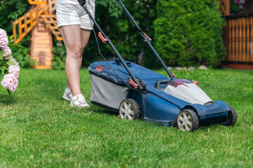 This image captures someone mowing their lawn with a push lawn mower. The person is holding onto...