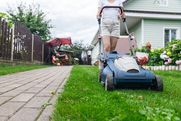 Person using a lawn mower to cut grass in a garden. The mower has a sturdy design with large wheels...