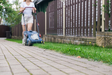 This image captures someone mowing their lawn with a push lawn mower. The person is holding onto...