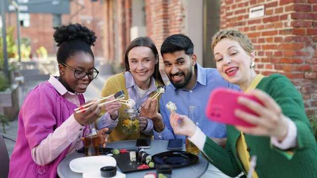 A diverse group of friends enjoys sushi and takes a selfie at an outdoor cafe.