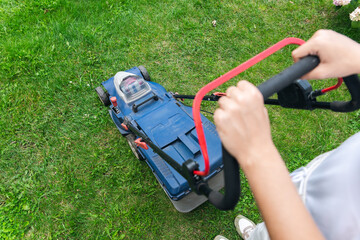This image captures someone mowing their lawn with a push lawn mower. The person is holding onto...