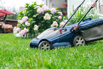 Lawn mower cutting green grass in backyard. Gardening background.