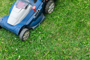 Lawn mower cutting green grass in backyard. Gardening background.