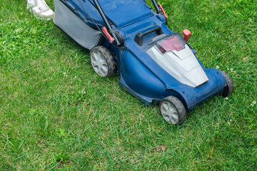 Lawn mower cutting green grass in backyard. Gardening background.