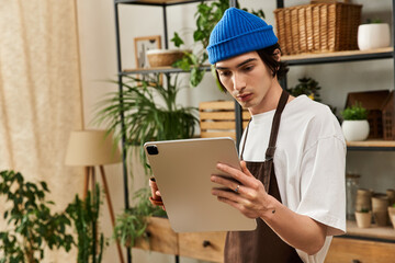 Handsome young man caring for plants and using a tablet in a stylish indoor garden studio