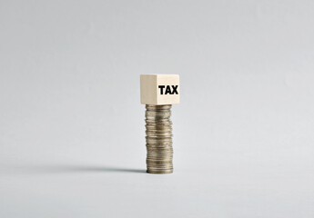 Stack of Coins Balancing a Wooden Cube with Tax Concept on White Background