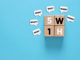 5W1H method on wooden cubes and speech bubbles representing questions on blue background