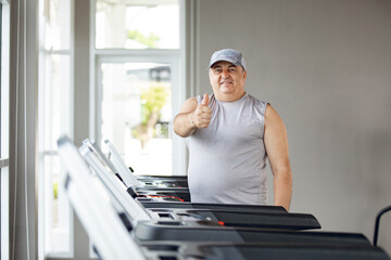 Man running on treadmills in sport gym .fitness man runner show Thumbs up on running machine in...
