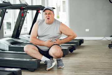 man at the gym with hand on stomach because nausea, painful disease feeling unwell. ache concept.