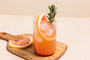 Grapefruit cocktail with rosemary garnish in a glass, served on a wooden cutting board. Vibrant,...