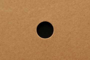 A solitary black dot stands out against the textured brown background of a cardboard surface