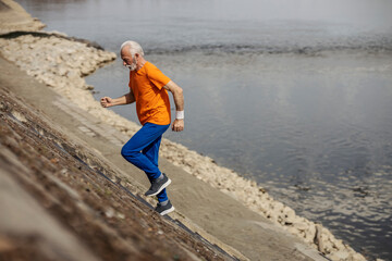 Full length senior sportsman running up stairs near river.