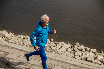 Top view of senior sportsman in shape running fast on riverbank.