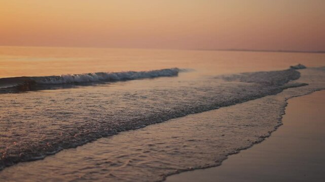 4K Slow motion shot of sea waves during the sunset at Mandvi beach in Mandvi, Kutch, Gujarat, India. Scenic view of calm beach waves of the Arabian sea during the golden hour. Water shines orange. 
