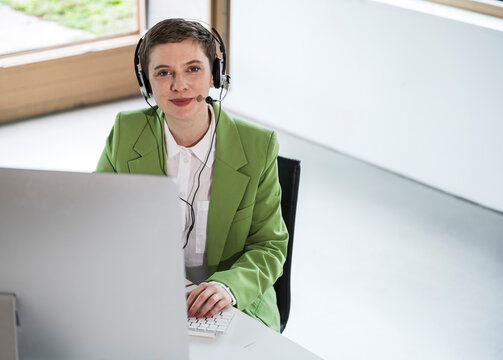 Businesswoman in green blazer with headset working at a computer in a modern office