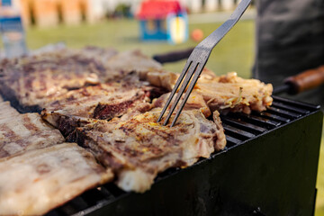 Close up of a grilling fork pressing roasted meat on a grill.