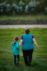Fototapeta premium Grandmother and granddaughter stroll hand-in-hand across a grassy field, enjoying a peaceful afternoon together.