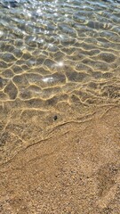 Crystal clear seawater gently washing over a golden sandy beach, revealing the natural texture beneath the surface, Porto Portugal. Close up	