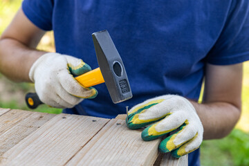 Hand holding a hammer to drive nails into the wood. Carpenter with hammer and nails fixes a wooden...