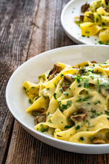 Papperdelle pasta with champignons mushrooms in cream sauce and parsley on wooden table	