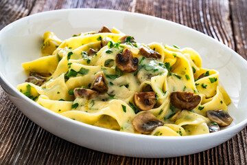Papperdelle pasta with champignons mushrooms in cream sauce and parsley on wooden table	