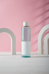 Blue transparent cosmetics bottle with blank sticker template, no brand mockup. Concrete decorative arches on pink background. Product advertising, copy space