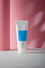 White blue cosmetics tube mockup, no brand template with paper roll on pink background with decorative shadows. Product advertising banner. Copy space