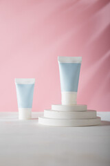 Tender blue cosmetics tubes on white concrete pedestal, pink background. Blank label, no brand logo template, mockup. Copy space. Product advertising banner