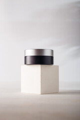 Silver black cream or eye patches jar with no brand, blank label mockup on concrete cube stand, white background. Product advertising banner, copy space