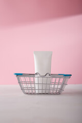 White cosmetics tube mockup template, no brand container in shopping basket on pink background. Online beauty product order concept. Copy space