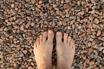 Bare feet of women on the street in summer on small stones on the road stand, movement, choice and...