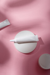 Two white narrow unbranded cosmetics tubes mockup on concrete stand, pink background. Beauty product template, advertising banner. Copy space. Flay lay, top view