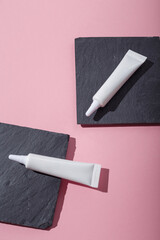 Two white narrow unbranded cosmetics tubes mockup on concrete stands, pink background. Beauty product template. Copy space. Flay lay, top view