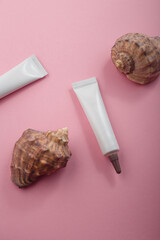 Two white narrow unbranded cosmetics tubes mockup, seashells on pink background. Beauty product template, advertising banner. Copy space, top view, flat lay
