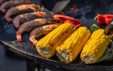 Close-up of corn and meat grilling on a barbecue. The corn is charred and golden, while the meat...