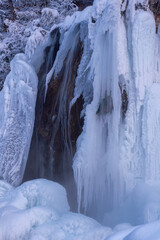 Majestic frozen waterfall cascading down rocky cliff, surrounded by icy formations and snow-covered landscape, showcasing the beauty of winter nature and tranquility © Denis Tuev