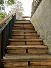 Old wooden staircase leading upward against a concrete wall.
Cracked paint and dust cover the walls.
Outdoor stair.