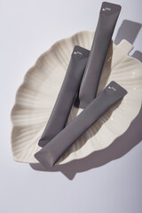 Some grey cosmetics sticks on leaf shaped plate and white background. Hair repair mask mockup, unbranded template, no label. Copy space